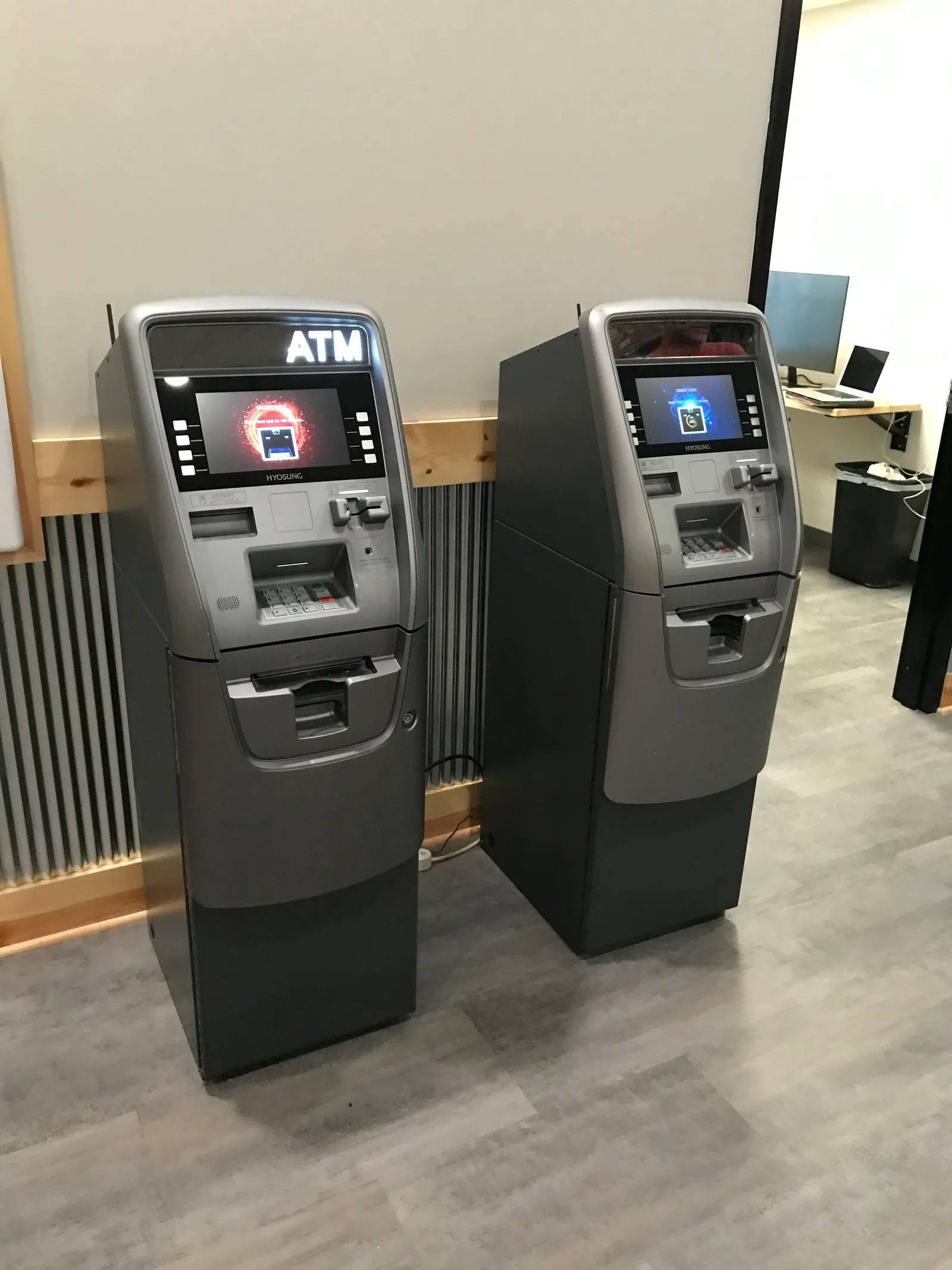 Two Envision ATM machines standing side by side in a bright office lobby